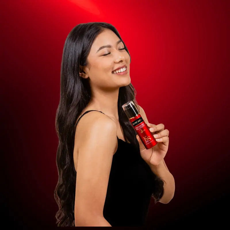 A woman holding a bottle of True Me Keratin Hair Serum against a red background.