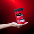 A hand holding a red container of True Me Hair Bleach Powder against a red background.